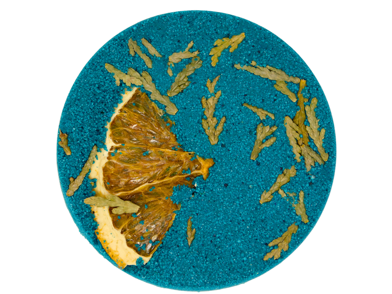 green circular bath bomb pressed with orange peel and cedar
