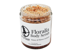 Sugar scrub with poppy seeds and earthy hue packaged in 8 oz glass jar with white label that reads: Floralia Body Scrub. Honey & Flower Garlands.