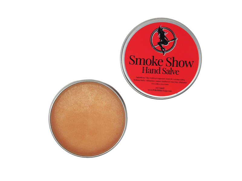 smoke show packagec in an aluminum 2 oz tin with the lid removed and placed to the side to show the pink/orange salve inside the tin. Lid has a red label that says Smoke Show Hand Salve and lists the ingredients.